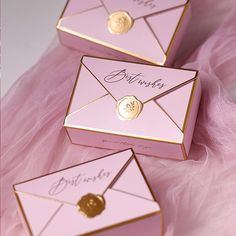 three pink envelopes with gold accents are sitting on a pink feathered bed sheet