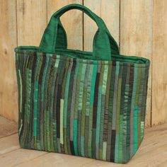 a green tote bag sitting on top of a wooden floor next to a fence