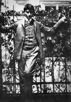 an old black and white photo of a man standing in front of a fence with his arms outstretched