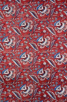 a red paisley print fabric with blue and white designs on it's edges,