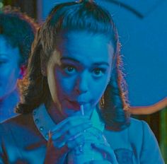 a young woman drinking from a plastic bottle in front of a blue neon light background