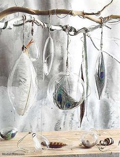 several glass ornaments hanging from a tree branch on a wooden table in front of a wall