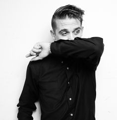 a man with his hands on his face posing for the camera while leaning against a wall