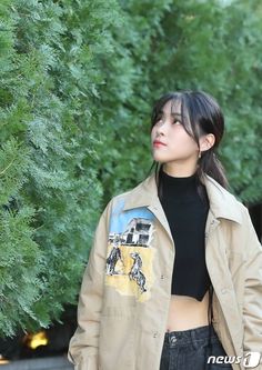 a woman standing in front of trees wearing a jacket and black top with an image on it