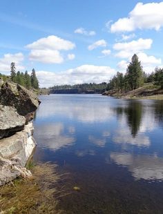 a lake surrounded by rocks and trees under a blue sky with clouds in the background