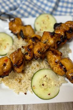 chicken skewers with cucumbers and rice are served on a white plate