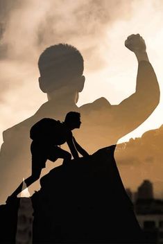 the silhouette of a man on top of a rock with his arm in the air