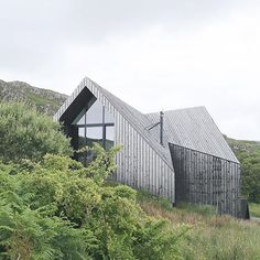 a wooden building sitting on the side of a lush green hillside next to tall grass