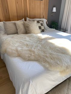 a bed with white fur on it in a bedroom next to a wooden headboard