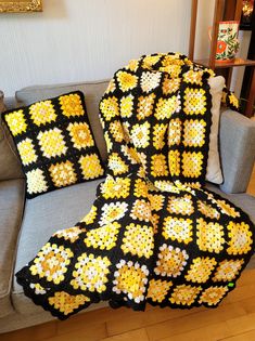 a crocheted granny blanket sitting on top of a couch next to two pillows