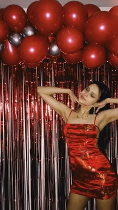 a woman standing in front of red and silver balloons with her arms behind her head