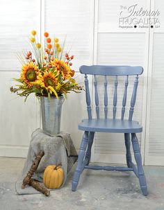 a blue chair next to a vase with sunflowers in it and a pumpkin