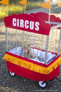 a child in a red wagon that says circus on the side and yellow flags behind it