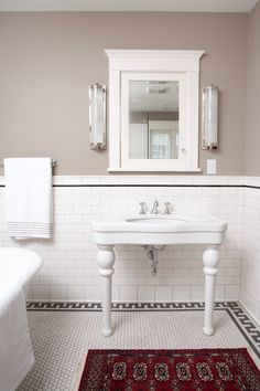 a white sink sitting under a bathroom mirror next to a bath tub and rug on the floor