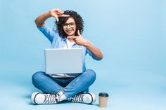 a woman is sitting on the floor with her laptop and pointing at something in front of her