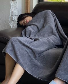 a woman is laying on a couch wrapped in a gray blanket and she has her eyes closed