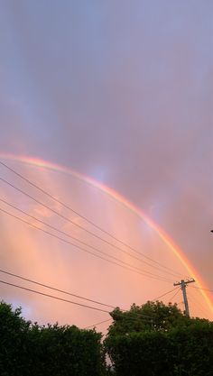 two rainbows in the sky with power lines and trees behind them at sunset or dawn