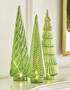 three green glass christmas trees sitting on top of a white mantle next to a mirror