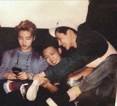 three young men sitting on a couch looking at their cell phones while laughing and holding each other's hands