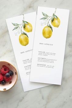 two lemons and raspberries on top of a table next to a bowl of berries