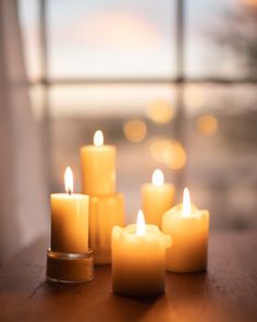 several lit candles sitting on top of a wooden table next to a large window in the background