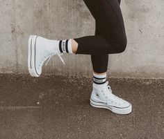 a person wearing white sneakers and black leggings standing in front of a concrete wall