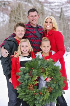 a group of people standing in the snow with a christmas wreath on their lap and smiling at the camera