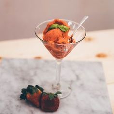 a glass filled with ice cream and two strawberries on top of a marble table