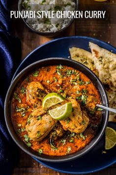 a blue plate topped with chicken curry next to naan bread and lime wedges