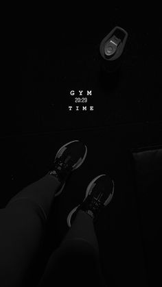 a person's legs and shoes on a black surface with the words gym time written in white