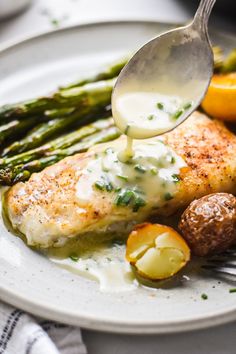 a plate with chicken, asparagus and potatoes being drizzled with sauce