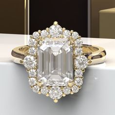 an emerald cut diamond surrounded by smaller round diamonds on a gold band, in front of a black and white background