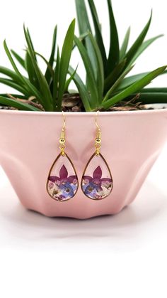 a pair of earrings sitting on top of a pink planter next to a potted plant