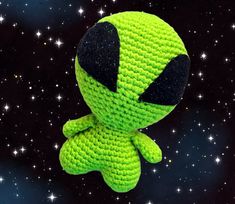 a green crocheted stuffed toy sitting in the middle of space with stars around it