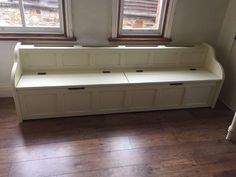 a white bench sitting in the corner of a room with two windows and wooden floors