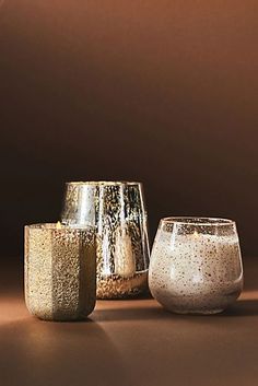 three gold and silver vases sitting on top of a brown table next to each other