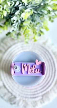 a purple name plate with the word mia on it sitting next to a green plant