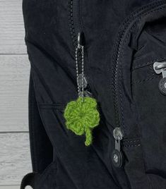 a green crochet keychain hanging from a black backpack on a white wooden background