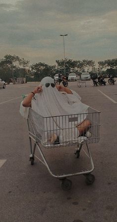 a person laying in a shopping cart covered with white cloth and sitting on the floor