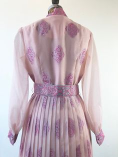 "1960's Alfred Shaheen pink oraganza maxi gown has an allover silver and pink foil print, with concentrated border motif at the hem and sleeve cuffs. There's a matching printed removable belt that has hooks and grommets for closure. The dress has a sunburst pleated skirt, unlined sheer bishop sleeves, and a button front and cuffs. The dress body is lined in a pink rayon that becomes an underslip in the skirt. Made in USA. 91% polyester, 9% nylon. Condition Excellent. Belt has wrinkling to vinyl Festive Vintage Pink Dress, Organza Maxi Dress, Alfred Shaheen, Pink Foil, Maxi Gown, Body Dress, Maxi Gowns, Green Print, Sweet Dress