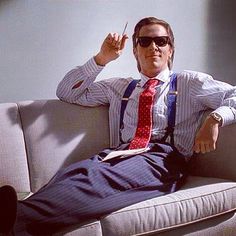 a man sitting on top of a couch wearing sunglasses and a tie with his hand up in the air