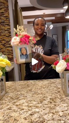 a woman standing in front of a counter with flowers and pictures on the counter top