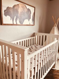 a white crib in a room with a painting on the wall and a teepee tent