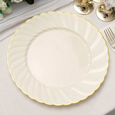 a white and gold plate on a table next to silverware, flowers and wine glasses