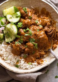 a bowl filled with rice and meat next to cucumbers