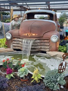 an old truck with water coming out of it's trunk and flowers in the front