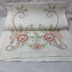 an embroidered tablecloth with flowers and vines on white linen, folded in two rows