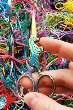 a person holding a pair of scissors in front of a pile of colorful yarns