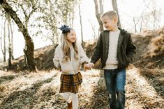 a young boy and girl holding hands walking through the woods