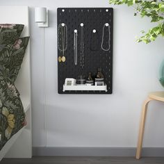 a wall mounted jewelry organizer on a white wall next to a green plant and chair